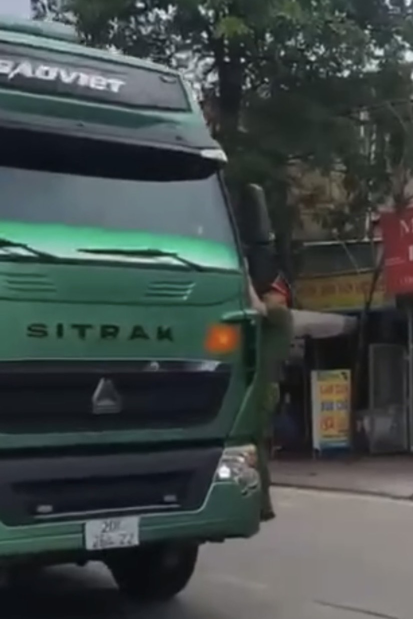 Hình ảnh Đại uý Nguyễn Đức Dũng đang đứng trước đầu xe phải nhảy lên bám vào gương bên lái để tránh không bị xe đâm.
